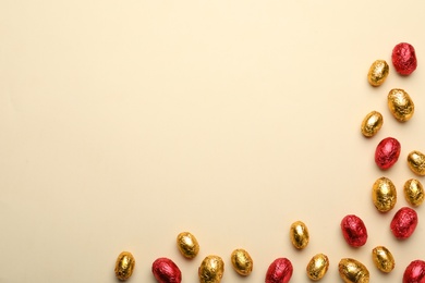 Photo of Chocolate eggs wrapped in red and golden foil on beige background, flat lay. Space for text