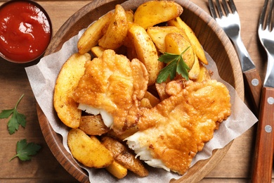 Photo of Wooden plate with British traditional fish and potato chips, top view