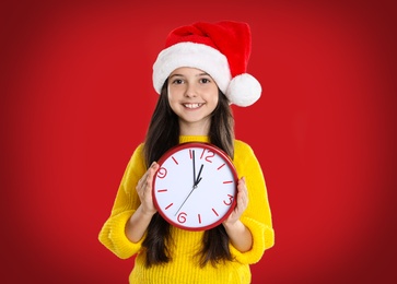 Photo of Girl in Santa hat with clock on red background. New Year countdown