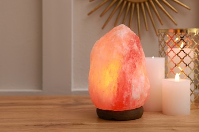 Photo of Himalayan salt lamp and candles on wooden table near white wall indoors, space for text