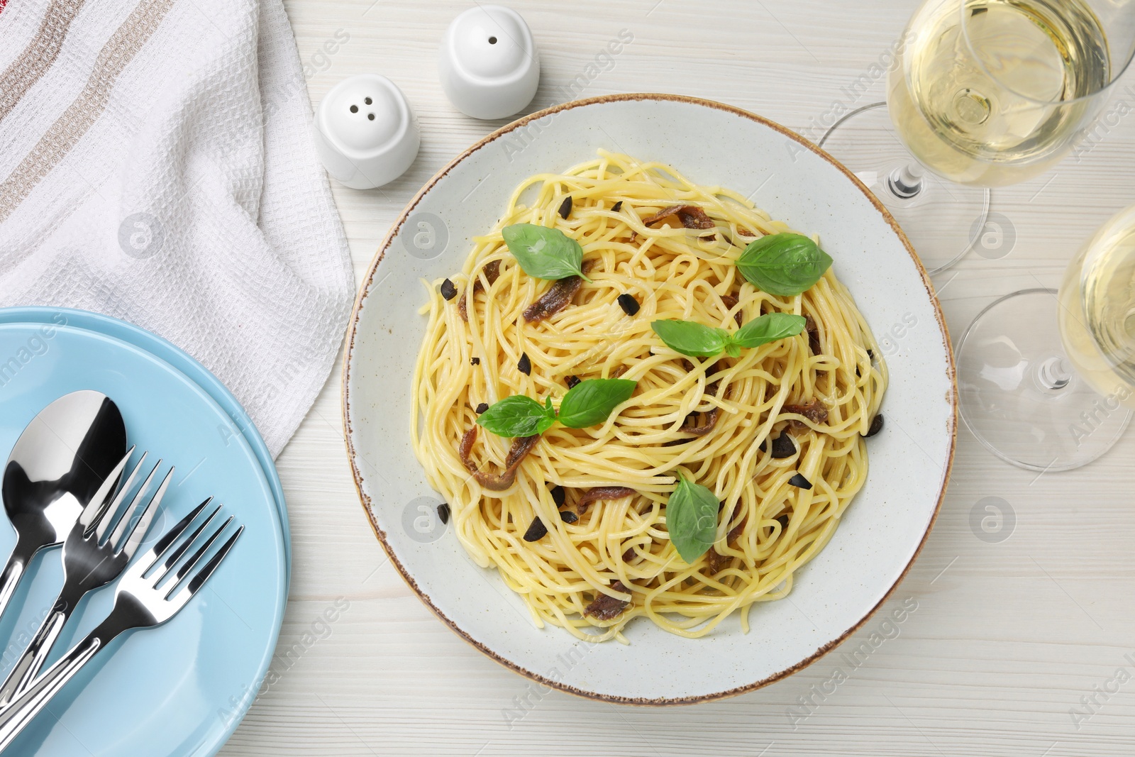 Photo of Delicious pasta with anchovies, glasses of drink and cutlery on white wooden table, flat lay
