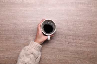 Woman with cup of coffee at wooden table, top view. Space for text