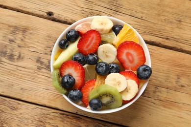 Tasty fruit salad in bowl on wooden table, top view