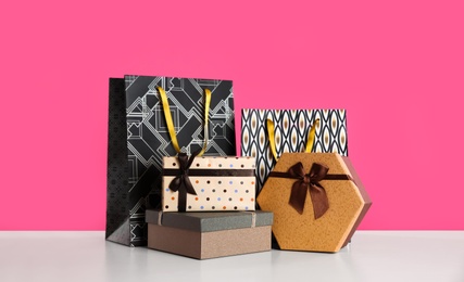 Photo of Gift bags and boxes on white table against pink background