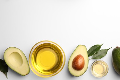 Photo of Cooking oil in bowl and fresh avocados on white background, flat lay. Space for text