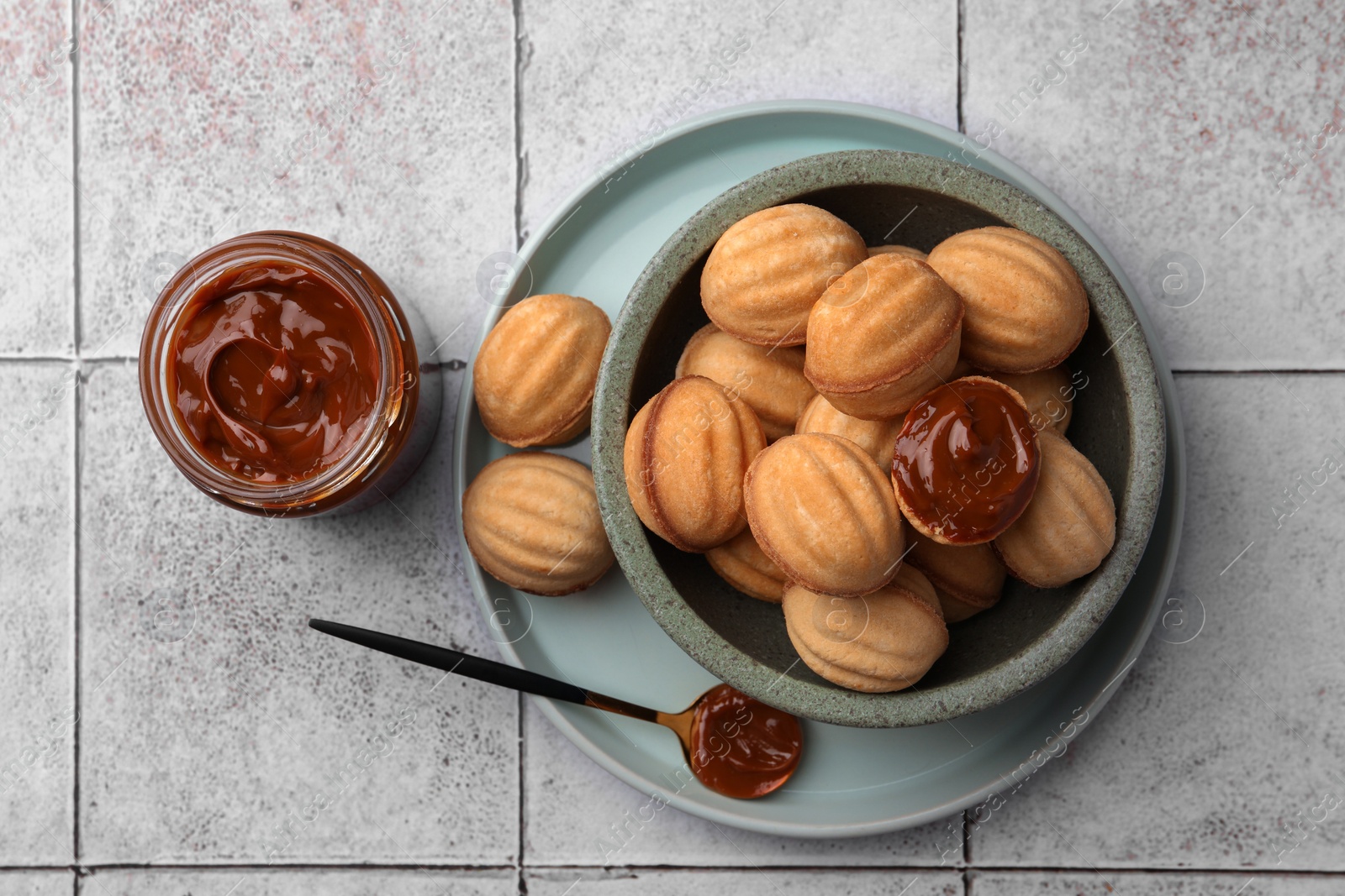 Photo of Delicious nut shaped cookies with boiled condensed milk on light textured table, flat lay