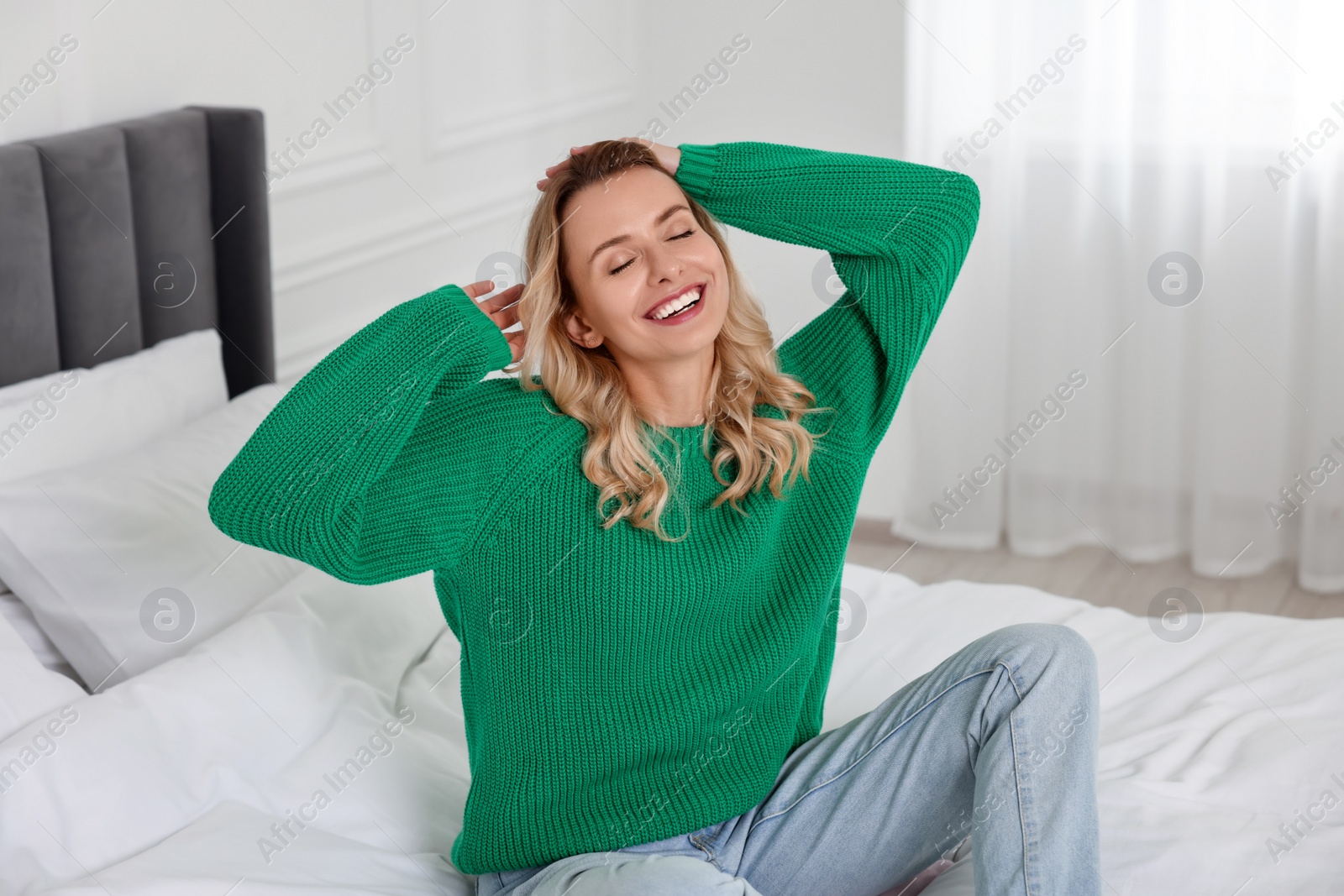 Photo of Happy woman in stylish warm sweater on bed at home