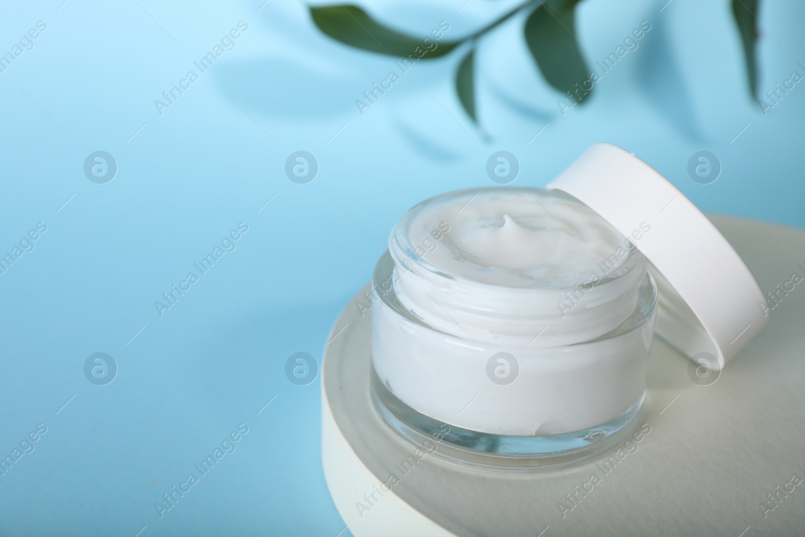 Photo of Jar of body cream with white stand on turquoise background, closeup. space for text