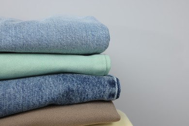 Stack of different folded clothes near grey wall, closeup. Space for text