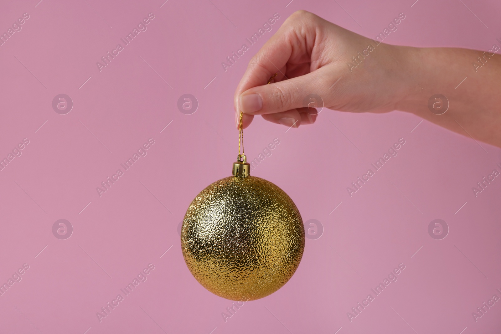 Photo of Woman holding golden Christmas ball on pink background, closeup. Space for text