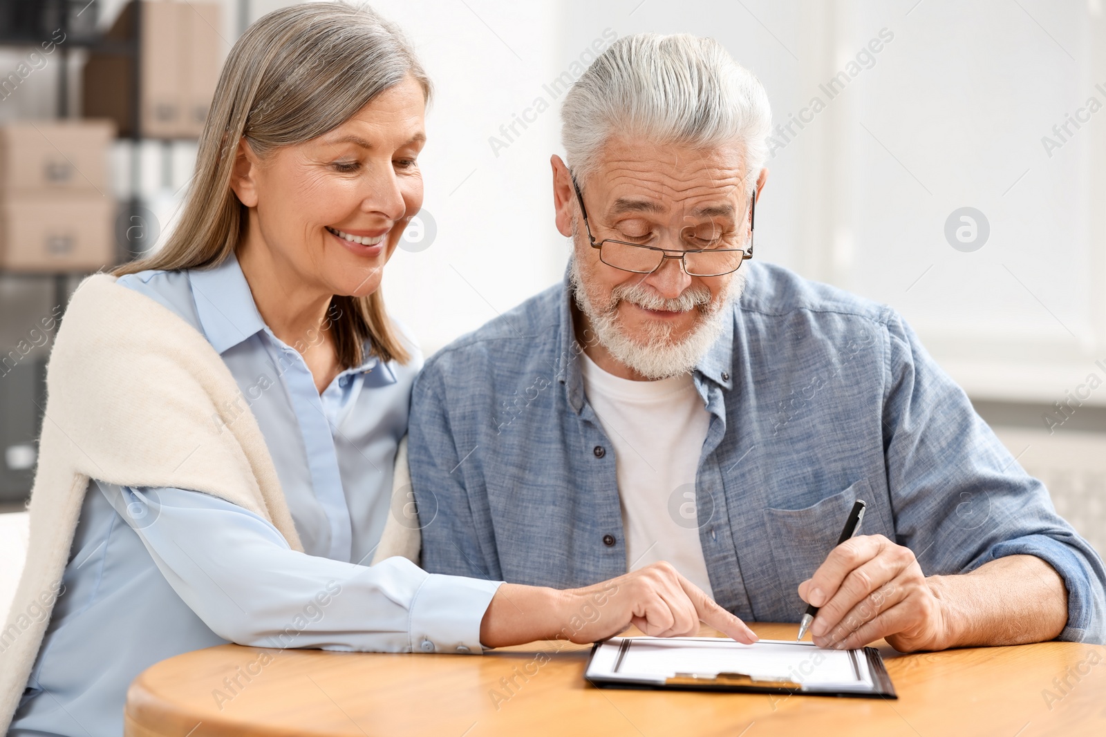 Photo of Happy senior couple signing Last Will and Testament indoors