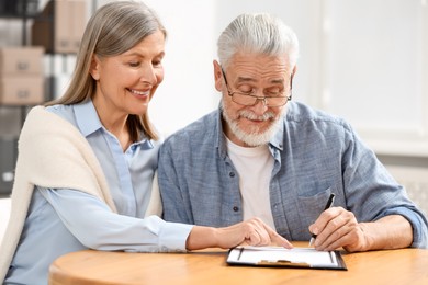 Photo of Happy senior couple signing Last Will and Testament indoors