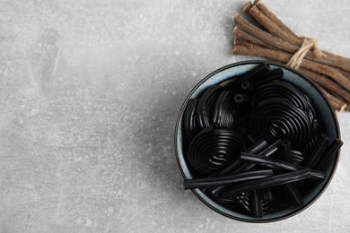Photo of Tasty black candies and dried sticks of liquorice root on grey table, flat lay. Space for text