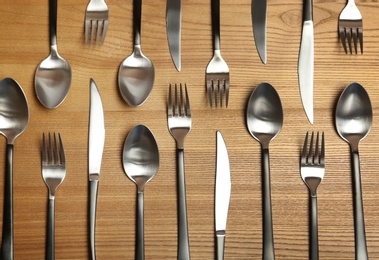 Photo of Forks, knives and spoons on wooden table, top view