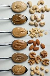 Tasty nut butters in spoons and raw nuts on white marble table, flat lay