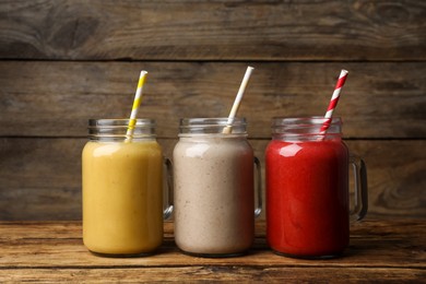 Photo of Mason jars with different tasty smoothies on wooden table