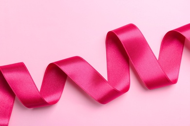 Simple pink ribbon on color background, top view