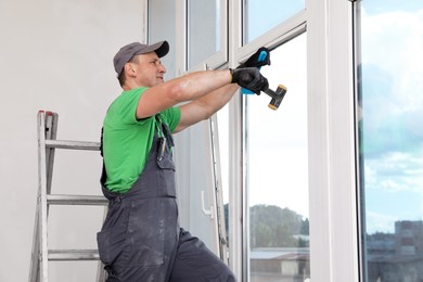 Worker in uniform installing double glazing window indoors