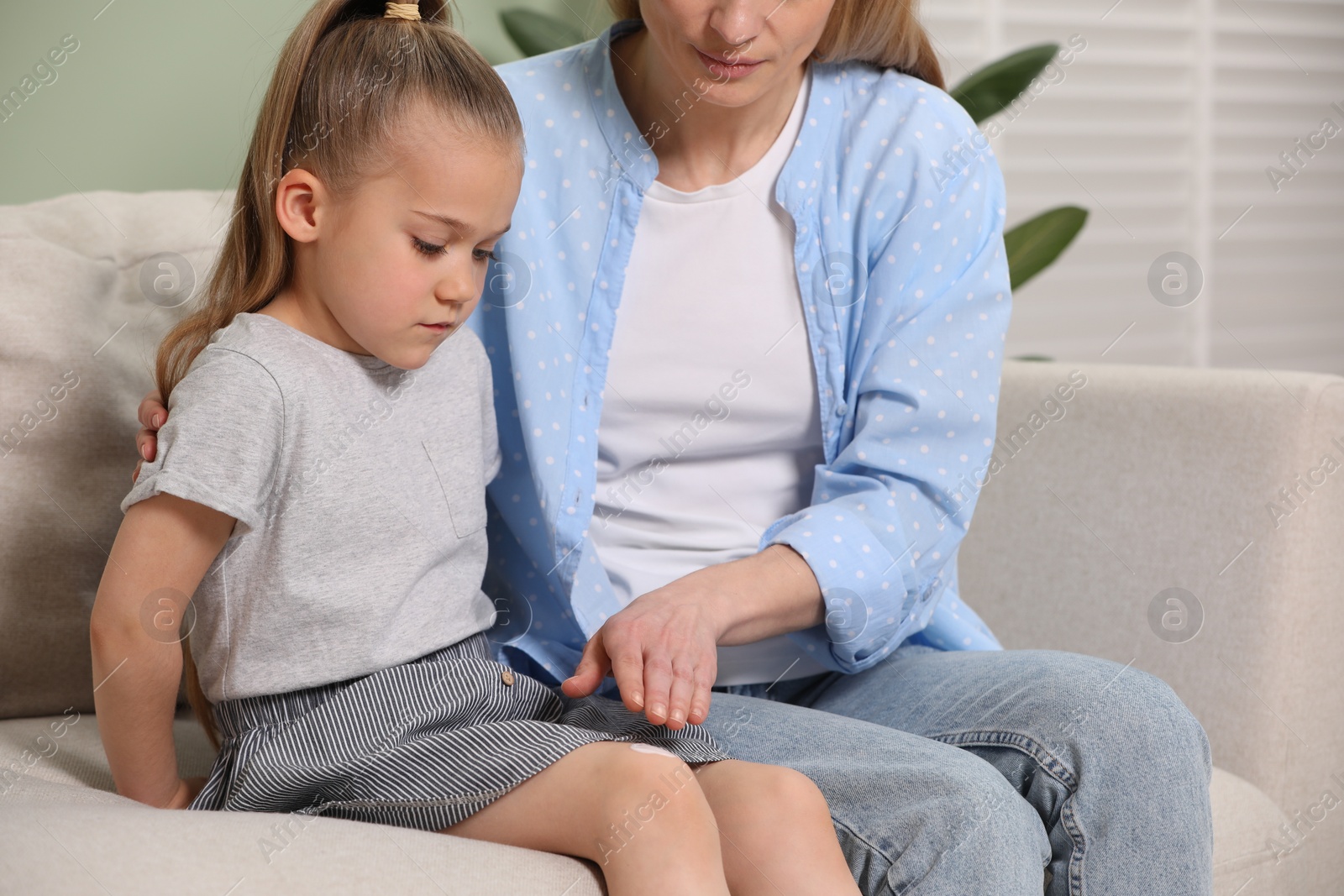 Photo of Mother applying ointment onto her daughter's knee on couch