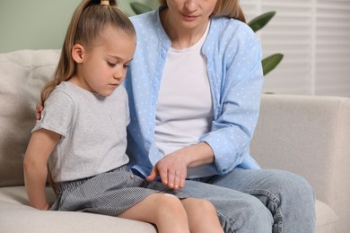 Photo of Mother applying ointment onto her daughter's knee on couch
