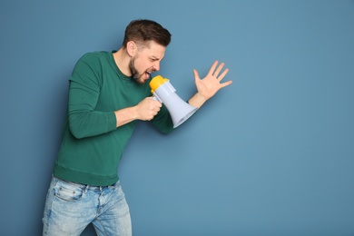 Photo of Young man shouting into megaphone on color background