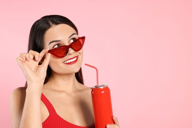 Photo of Beautiful young woman with stylish sunglasses drinking from tin can on pink background. Space for text