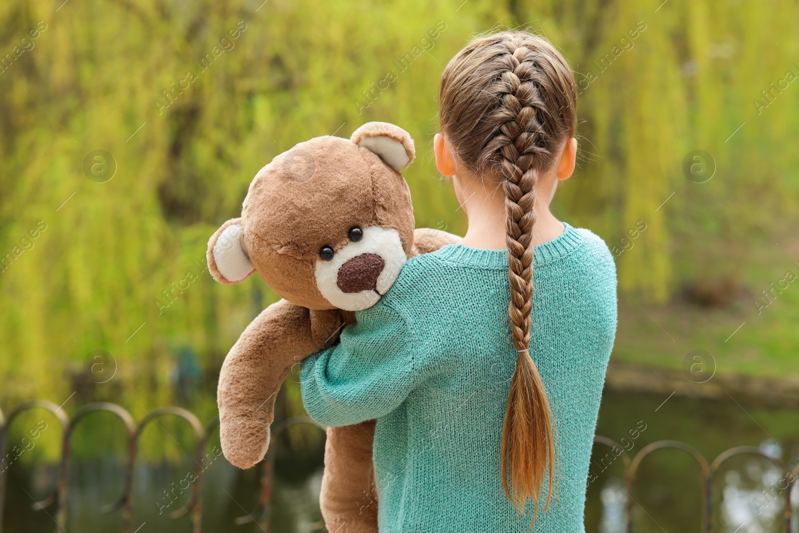 Photo of Little girl with teddy bear outdoors, back view