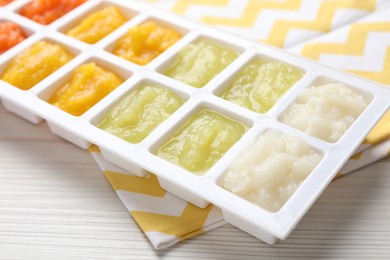 Photo of Different purees in ice cube tray on white wooden table, closeup. Ready for freezing