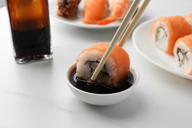 Dipping tasty sushi roll with salmon into soy sauce on white table, closeup