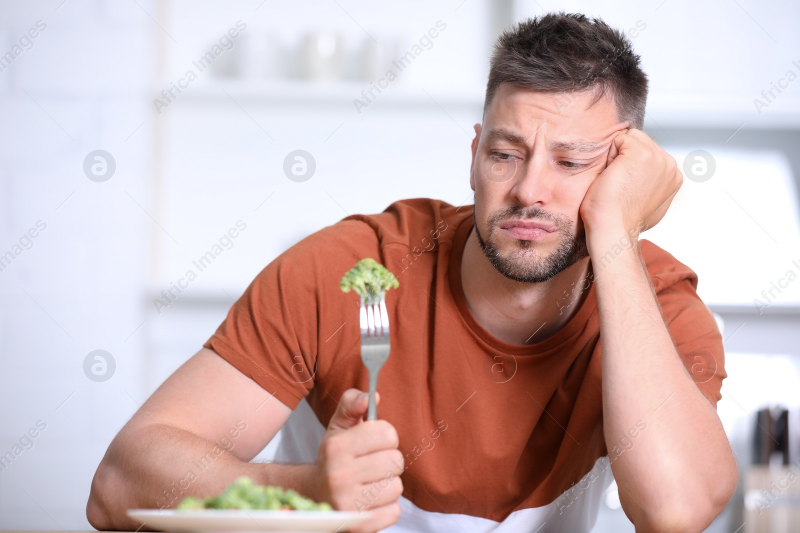 Photo of Portrait of unhappy man eating broccoli salad in kitchen