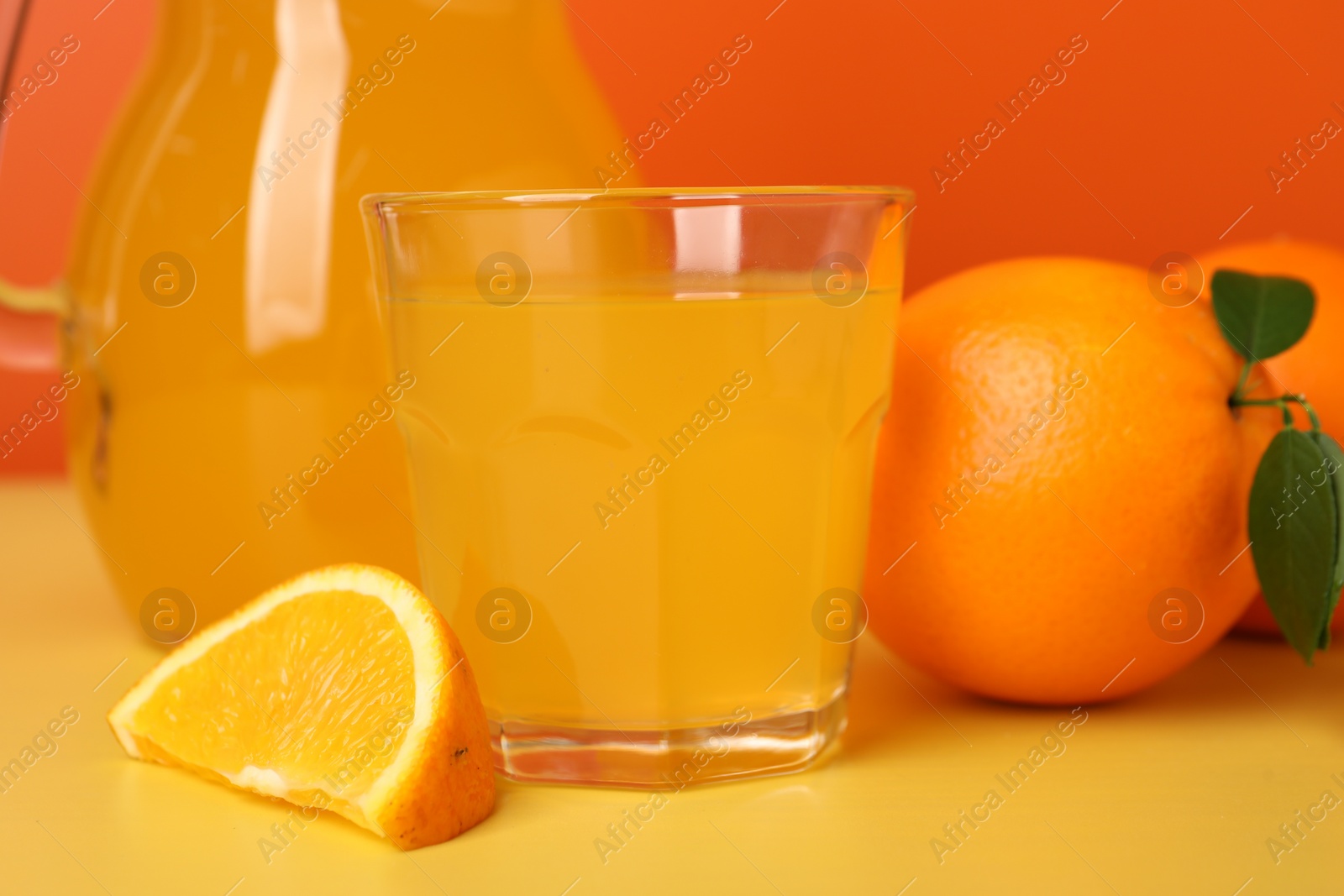 Photo of Glass of orange juice and fruit on yellow table, closeup