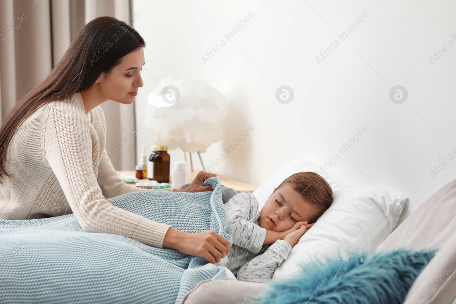 Photo of Mother taking care of her little son suffering from cold in bed