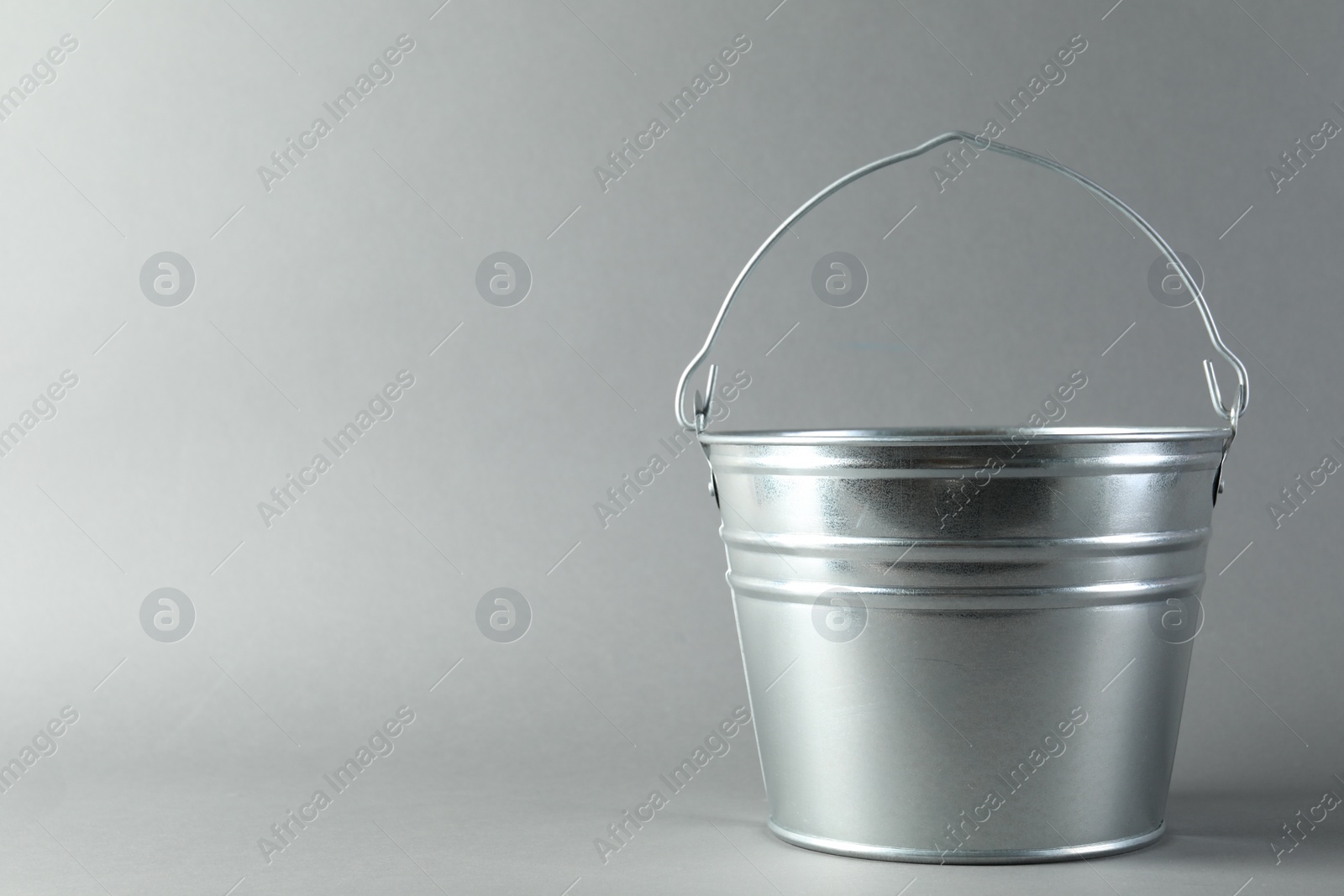 Photo of One shiny metal bucket on light grey background. Space for text