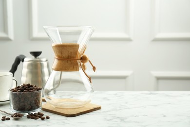 Photo of Glass chemex coffeemaker, kettle and beans on white marble table, space for text