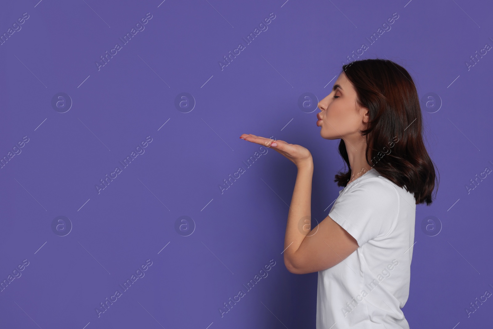 Photo of Beautiful young woman blowing kiss on purple background. Space for text