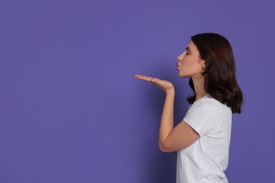 Beautiful young woman blowing kiss on purple background. Space for text