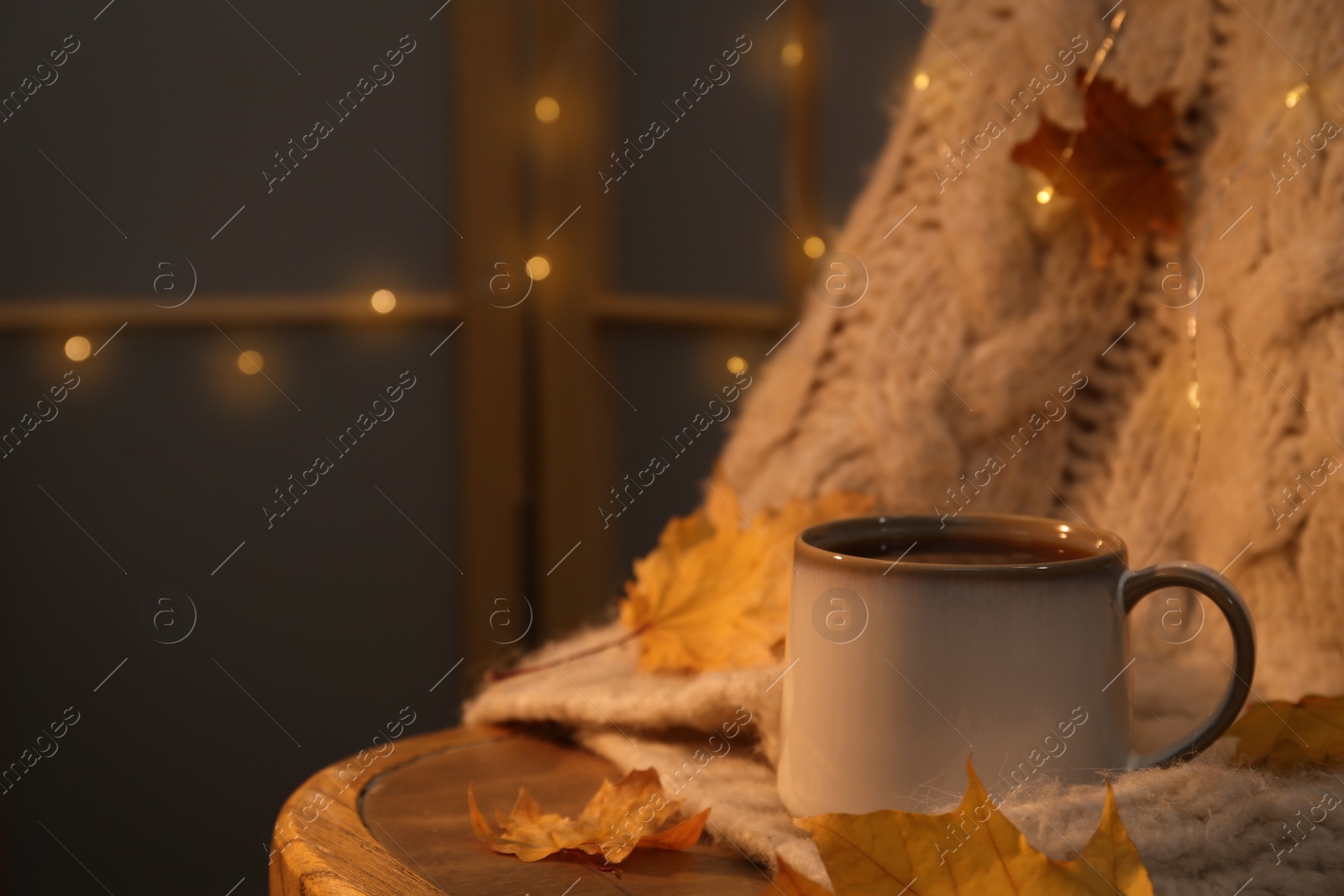 Photo of Cup of aromatic tea, sweater and autumn leaves on wooden chair indoors, space for text