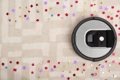 Photo of Modern robotic vacuum cleaner removing confetti from carpet, top view. Space for text