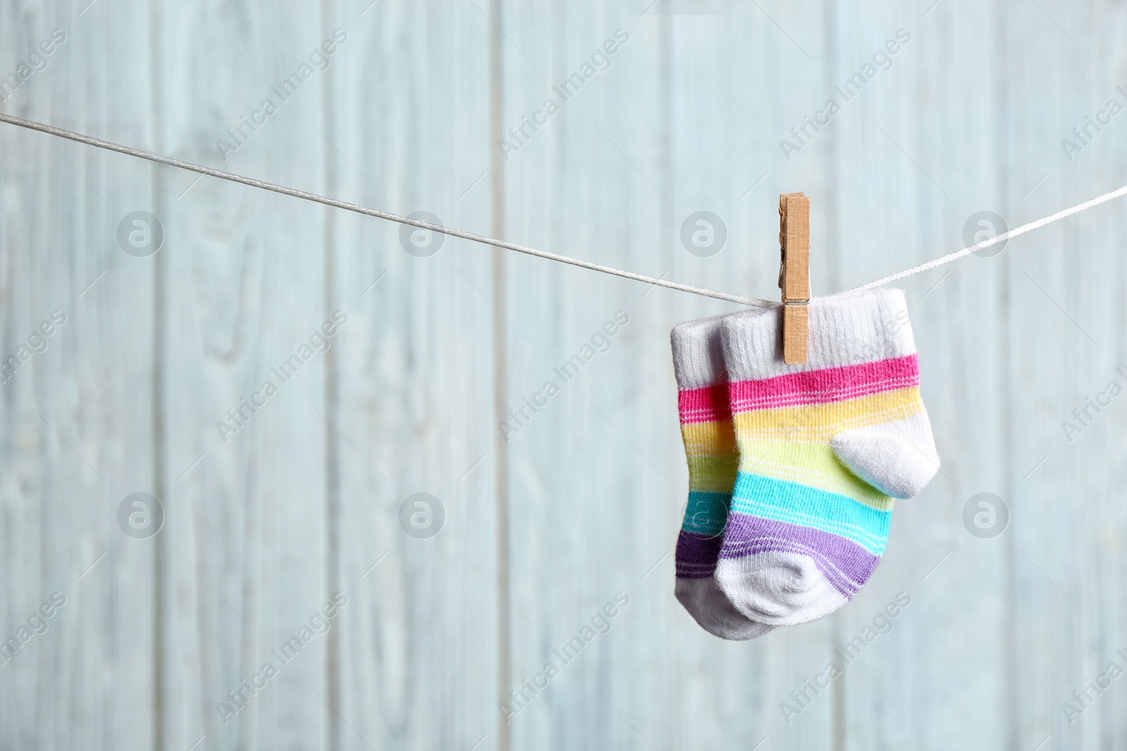 Photo of Pair of socks on laundry line against wooden background, space for text. Baby accessories