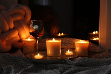 Photo of Glass of wine and burning candles on blanket in darkness