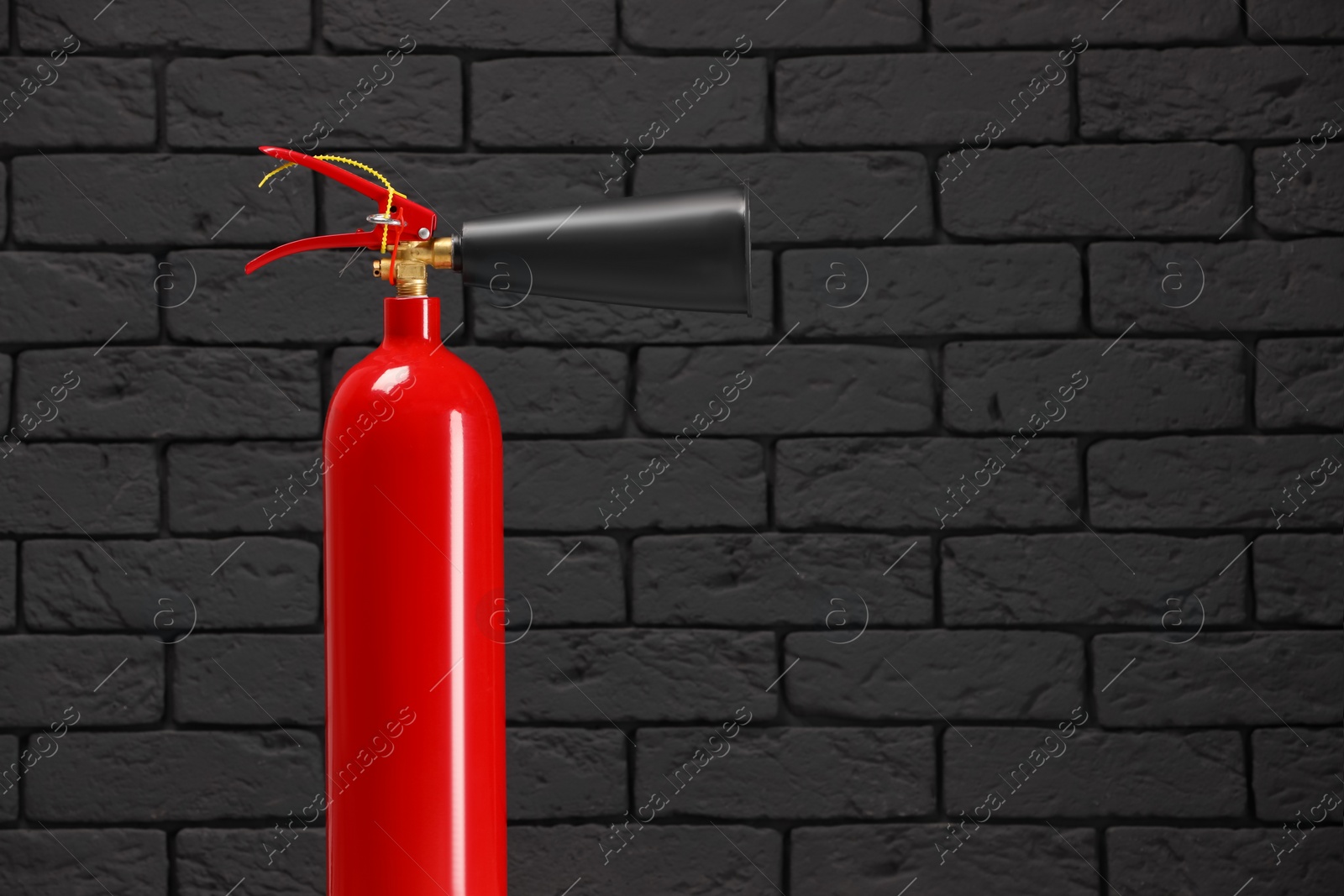Photo of Fire extinguisher against grey brick wall, space for text