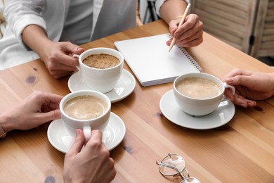 Photo of Women with cups of coffee at table in cafe, closeup