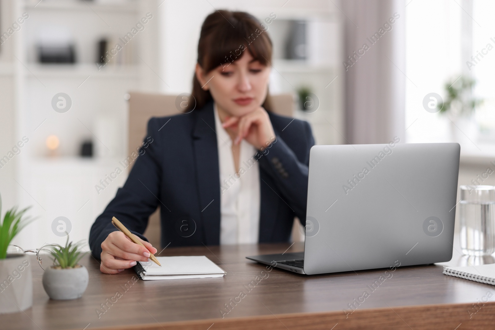 Photo of Woman taking notes during webinar at wooden table indoors