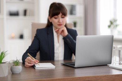 Woman taking notes during webinar at wooden table indoors