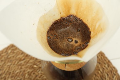Photo of Paper filter with aromatic drip coffee in glass chemex coffeemaker on table, closeup