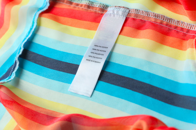 Photo of Clothing label with content information on colorful striped garment, closeup