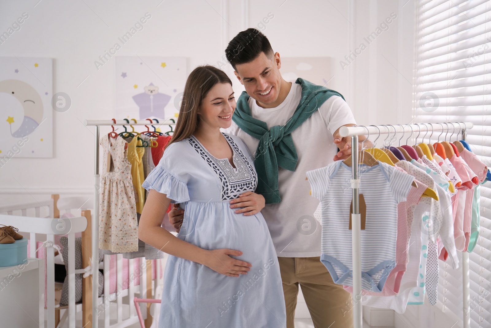 Photo of Happy pregnant woman with her husband choosing baby clothes in store. Shopping concept