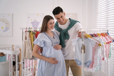 Happy pregnant woman with her husband choosing baby clothes in store. Shopping concept