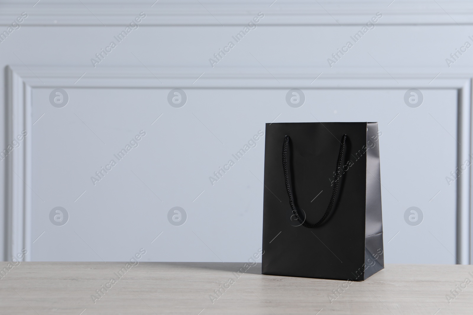 Photo of Black paper bag on wooden table against light grey wall, space for text