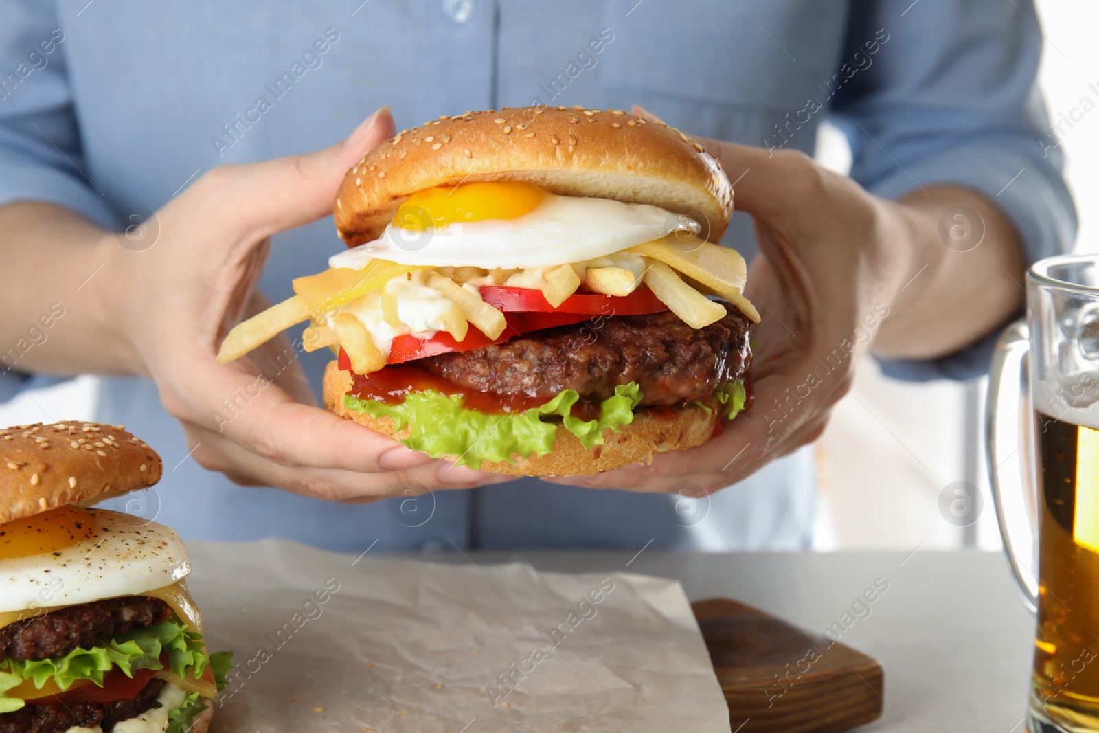 Photo of Woman holding tasty burger with fried egg over table, closeup